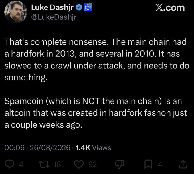 A tweet from Luke Dashjr (@LukeDashjr) dated 26/08/2026 arguing that the main Bitcoin chain had hardforks in 2010 and 2013 and has slowed under attack, while calling "Spamcoin" an altcoin from a recent hardfork—not the main chain—contextualizing his rebuttal to critics who call his Bitcoin definition "delusional."