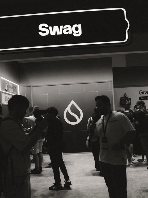 Attendees gather at the Sui Network booth at Basecamp, beneath a glowing "Swag" sign and the prominent Sui water-drop logo, capturing the lively atmosphere of the crypto conference.