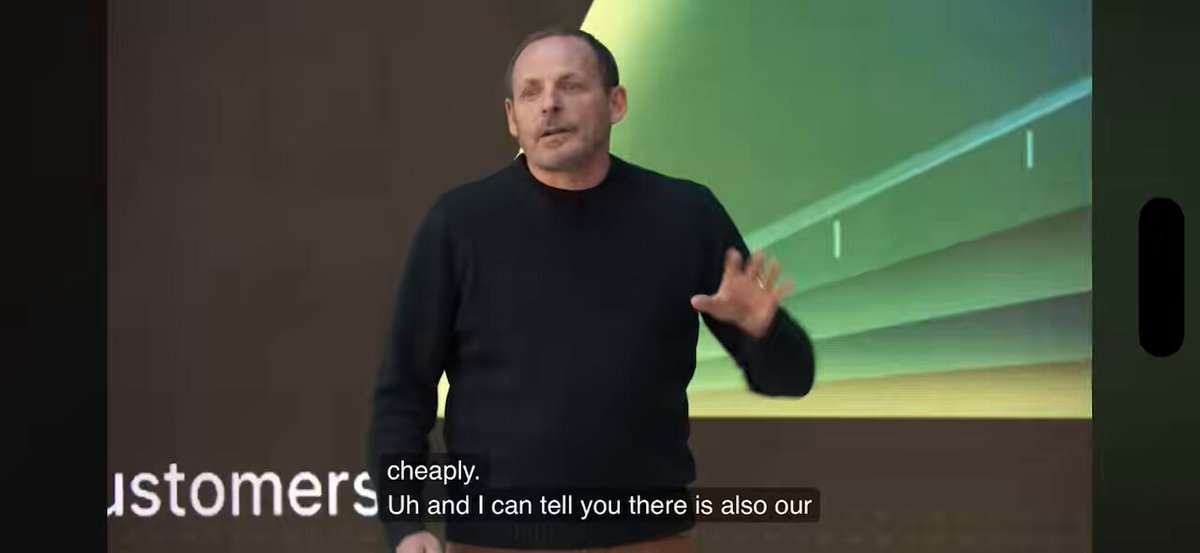 The image features a man standing in front of a screen, giving a presentation or speech. The background of the image is white with some green elements, possibly representing a slide from a presentation. The text "Customers" is written at the top left corner of the image, and there are two lines of text below it that read: "I'm sorry I can't tell you there's also our." This suggests that the man might be discussing a topic related to customers or their experiences with a company.