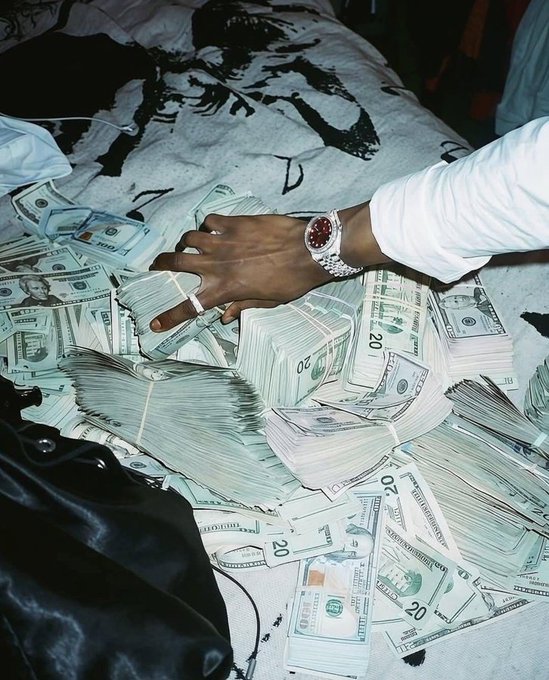 A person's hand resting on a bed covered with numerous stacks and loose $20 bills.