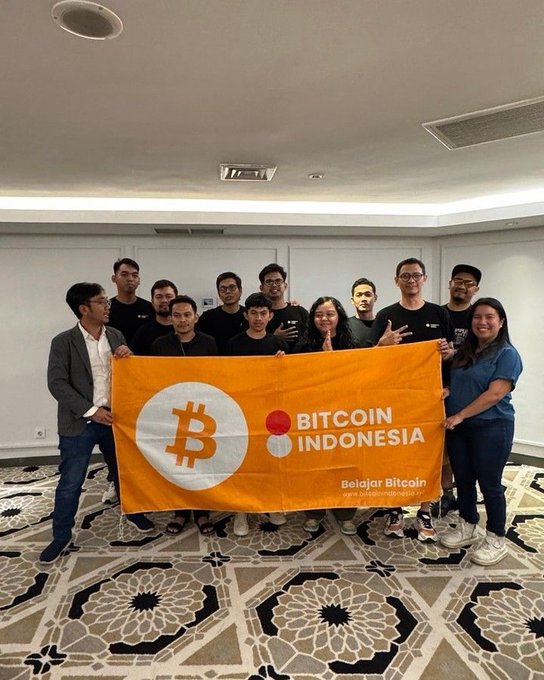 A group photo of young people holding a 'BITCOIN INDONESIA - Belajar Bitcoin' banner with the Bitcoin logo, likely taken at a crypto meetup event.