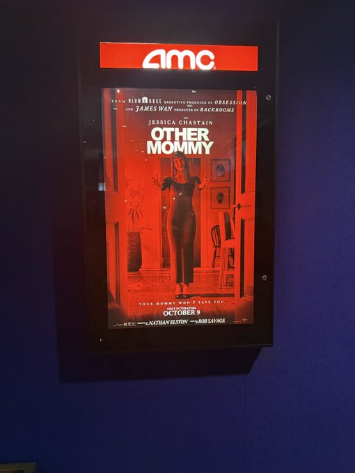 AMC theater display case showing the movie poster for 'OTHER MOMMY' starring Jessica Chastain, opening October 9, with red-toned artwork.