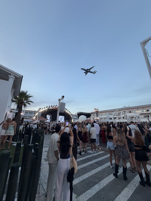 A diverse crowd gathers in Singapore to watch an airplane fly overhead, many holding up phones to capture the moment. The scene visually reinforces the post's sarcasm, highlighting how the crypto community was distracted by spectacle rather than focusing on meaningful user adoption in a vibrant, real-world setting.
