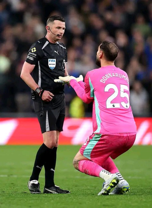 A FIFA referee speaking with goalkeeper Gianluigi Donnarumma (#25) in a pink Milan kit during a match.