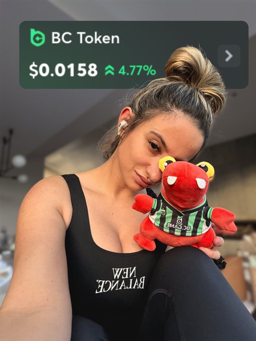 A woman holds a red plush mascot wearing a green and black striped "BC.GAME" shirt, with an overlay showing "BC Token" at $0.0158, up 4.77%.