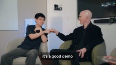 The image shows two men seated in chairs against a white wall, bumping fists together in what appears to be a casual setting, with the caption "it's a good demo" displayed at the bottom. The gesture suggests a moment of camaraderie or agreement, fitting the context of the "Virtuals Brian" post, possibly referring to a successful demonstration of virtual or AI technology.