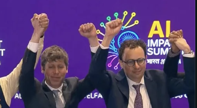A photo of two men in suits raising their hands in celebration at the AI Impact Summit, with a colorful logo visible in the background.