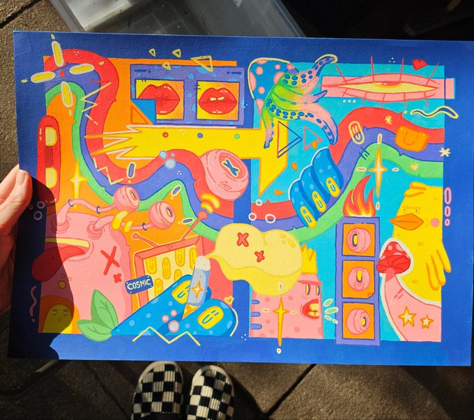 A vibrant, colorful abstract painting on blue paper featuring lips, butterflies, and various whimsical shapes, held up outdoors above checkered shoes.