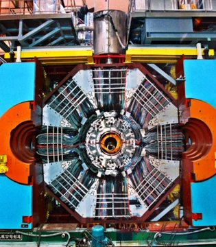An industrial overhead view of a large circular mechanical device, possibly a turbine or generator, with metal scaffolding and orange components.