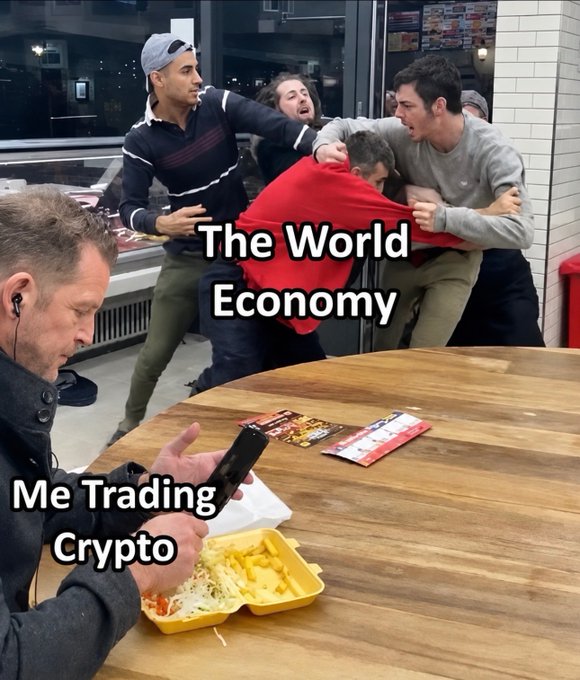 A meme showing a man labeled 'Me Trading Crypto' calmly eating fries and looking at his phone while four men in the background fight aggressively, labeled 'The World Economy'.