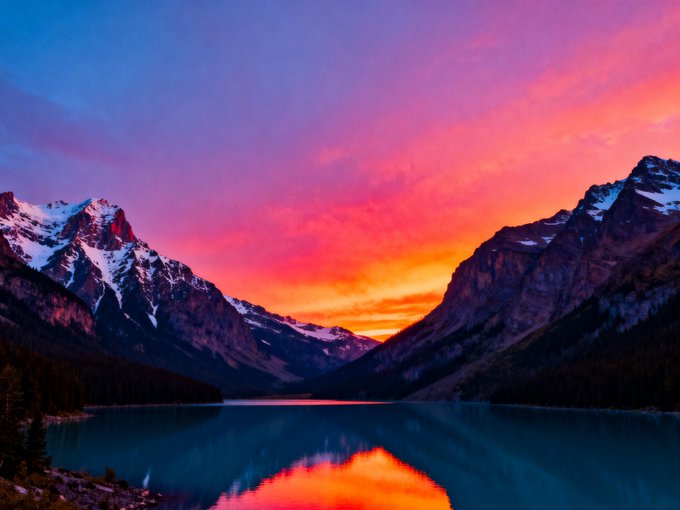 A vibrant sunset paints the sky in brilliant pinks and oranges, reflecting perfectly off a serene alpine lake nestled between snow-capped mountain peaks. The image captures the tranquil beauty of nature at twilight, embodying the peaceful horizon suggested by its NFT title.