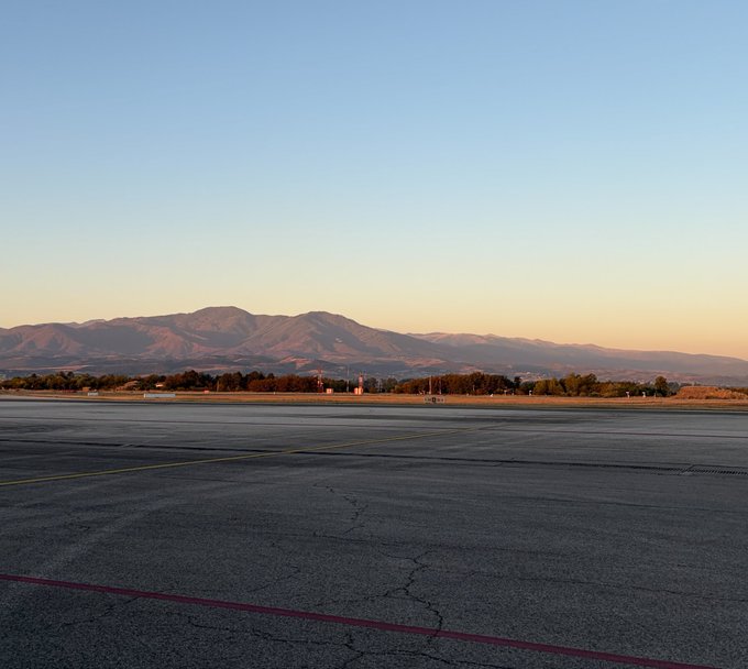 A scenic view of an empty airport tarmac with mountains in the background under a clear sky at sunset.