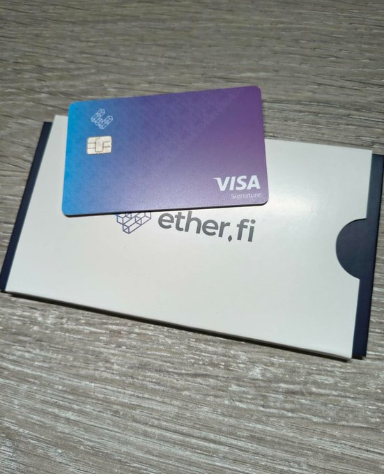 A Visa Signature debit card with a purple and blue gradient resting on top of a white 'ether.fi' branded envelope on a wooden surface.