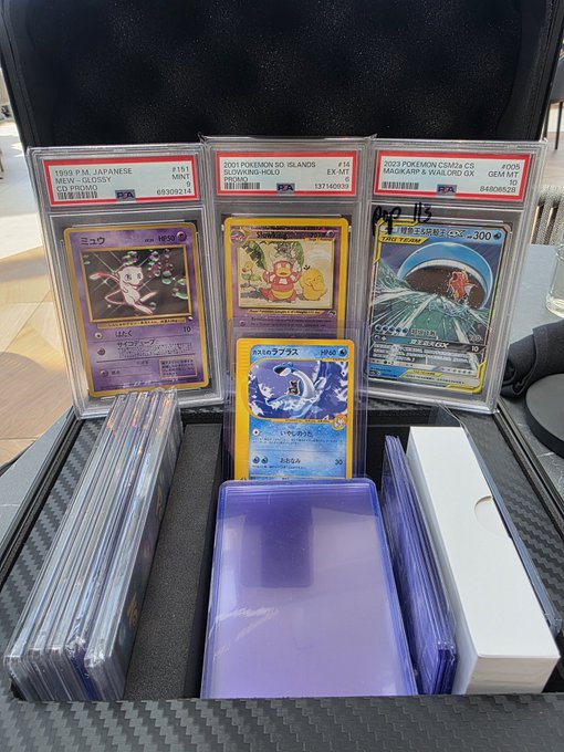 A collector's display of PSA-graded Pokémon cards including 1999 Japanese CD Promo Mew Glossy, 2001 Slowking-Holo Promo, and 2023 Magikarp & Wailord GX, along with a loose Japanese card and rows of ungraded cards in cases.
