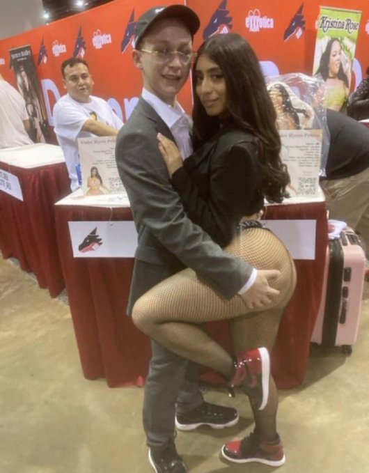 A young couple poses suggestively in front of booths promoting "Erotica" and "Kristina Rose". The image's provocative nature and the context of the post "Memecoin KOLs be like:" imply that KOLs (Key Opinion Leaders) in the memecoin space might engage in attention-grabbing or controversial behavior.