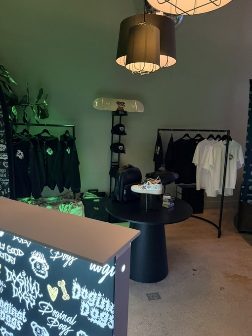 A clothing store interior featuring a black counter with 'Original Style' graffiti-style graphics, racks of black and white apparel, and pendant lighting.