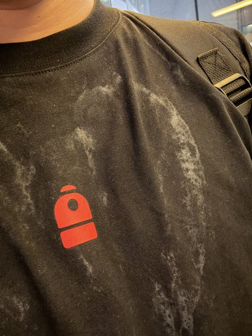 A close-up photo shows a person wearing a heavily worn, dark t-shirt with a red logo, carrying a bag strap over their shoulder.