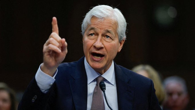 The image features a man wearing a suit and tie standing at a podium, giving an impassioned speech or lecture. The caption above him reads "Jaime Dimon is a Loser. 1. Shorted Saylor' s calls to embrace Bitcoin. 2. Rejected Saylor' $MSTR 3. Financed Epstein' s pedophile activities. 4. Debanked many people like Trump, Jack Mallers, etc. 5. Trying to stop the Clarity Act." The man's gesture and facial expression suggest that he is making a point or expressing his opinion on a particular topic.