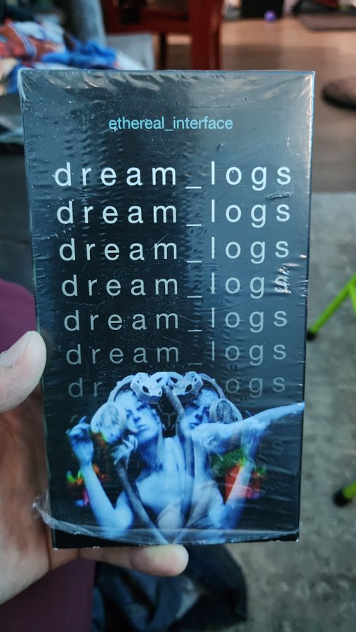 A hand holding a packaged item titled 'ethereal_interface / dream_logs' featuring blue-tinted classical statue imagery under plastic wrap.