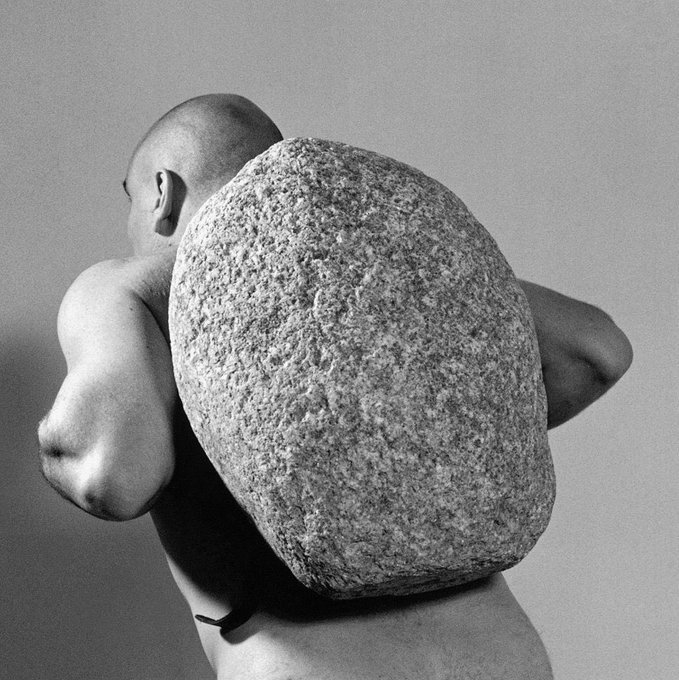 The image features a man wearing only his underwear, holding a large rock on his back against a white wall. The photo has been edited or altered to include text that reads "Another week with base network on my fucking back." This suggests that the image is related to a discussion about the concept of "base networks" in relation to the internet and social media usage.