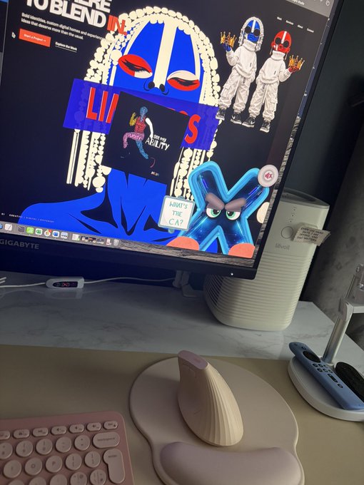 A desk setup featuring a Gigabyte monitor displaying colorful digital artwork, alongside a pink keyboard, a wooden ergonomic mouse, and a Lenovo PC tower.