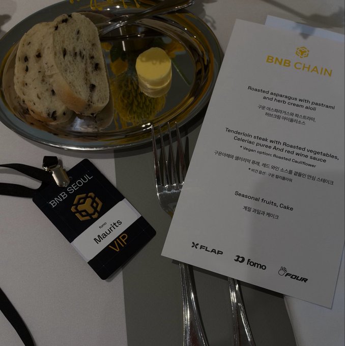 A BNB Chain VIP event place setting with a menu card listing items like 'Roasted asparagus with pastrami and herb cream aioli' and 'Tenderloin steak', alongside a plate of bread and butter, branded by 'X FLAP, fomo, FOUR'.