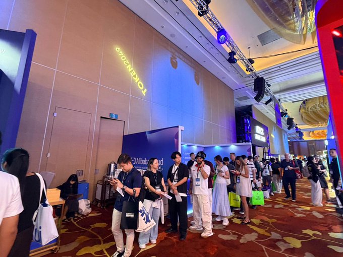 A bustling queue forms at the HTX Ventures booth on the floor of TOKEN2049, where attendees gather beneath the event's illuminated branding on the wall. Visitors browse merchandise and engage with staff in front of the "Global" display, illustrating the lively atmosphere and high foot traffic captured in the post.