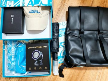 A Deepcoin × Argentina themed gift box containing a "VIAJANDO POR ARGENTINA" fanny pack, "CIRCULATING FAN", and a "DEEP COIN" branded umbrella, alongside a black leather backpack, celebrating Argentina's 2:1 World Cup victory over England.