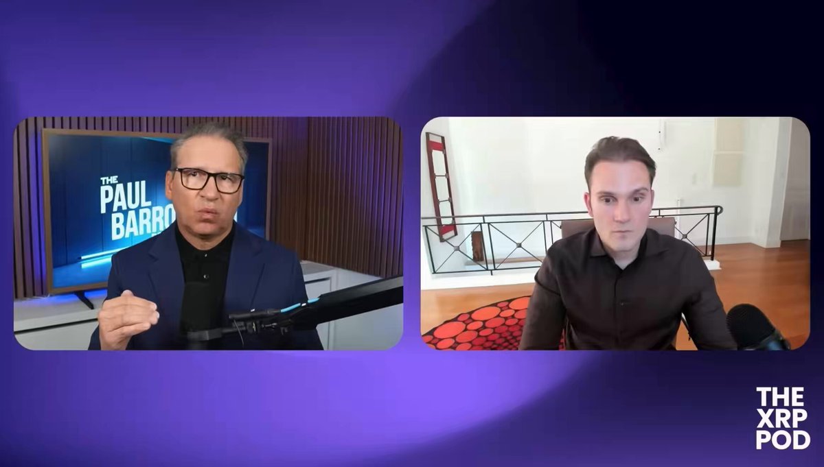 The image shows two men sitting behind a table with microphones, appearing to be having a conversation or participating in an interview. The background features a purple wall that has a TV screen mounted above it, displaying "The Paul Barro" logo.