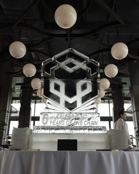 An indoor venue decorated with spherical hanging lights and an ice sculpture that reads '6 YEARS OF ON-BNB CHAIN' featuring the BNB logo.