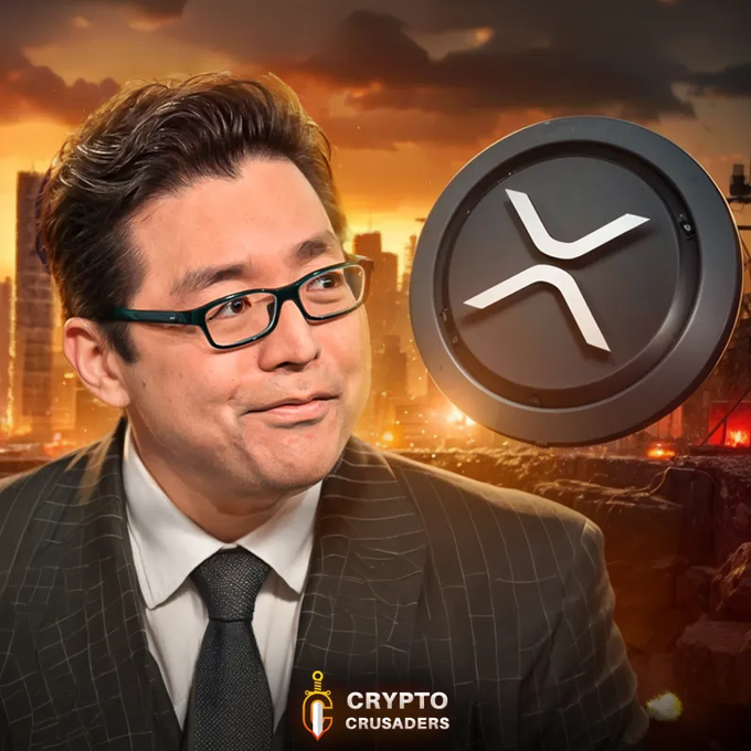 The image features a man wearing glasses, a suit, and a tie standing next to a coin with an X on it. The background of the image shows a city skyline at sunset, creating a dramatic atmosphere. The caption below the image reads "BOOOOOOOOMMM!!!! TOM LEE JUST SAID WE ARE ABOUT TO SEE ONE OF THE BEST RETURNS OF OUR LIFETIME!!! IT'S COMING $XRP". This suggests that the man is promoting Bitcoin or cryptocurrency, possibly as a result of an event or promotion.