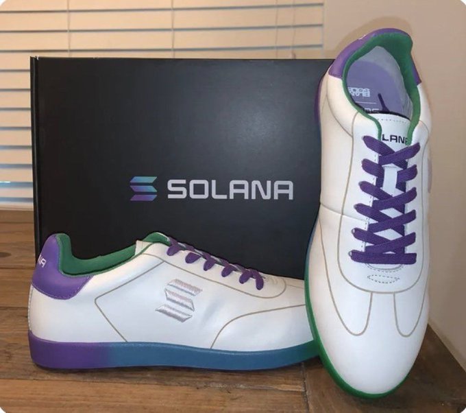 A pair of white sneakers with purple and green accents sits in front of a black "SOLANA" branded box, with "SOLANA" and "LANA" text visible on the shoes. The post humorously requests these Solana-branded sneakers as a birthday gift, with "$SOL" referencing the cryptocurrency ticker.