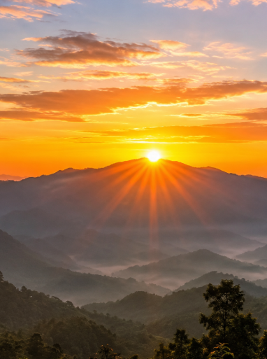 A stunning sunrise over mist-covered mountain ranges, with the sun's golden rays radiating across layers of hazy blue-green peaks.
