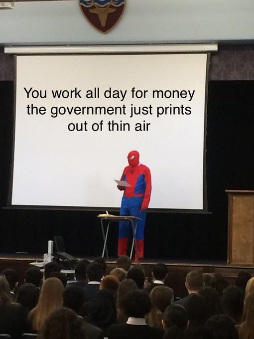 A person in a Spider-Man costume stands at a podium in front of an audience, with a projection screen behind them reading 'You work all day for money the government just prints out of thin air'.