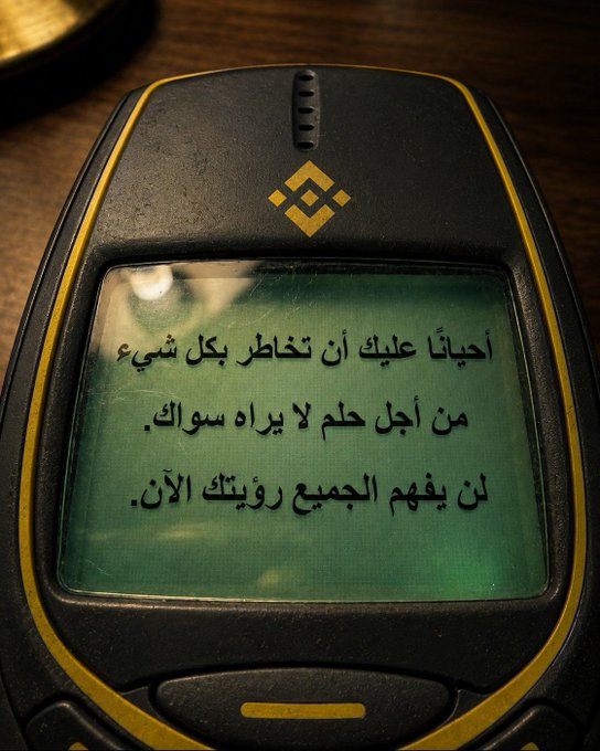 A black Nokia phone with a yellow border and logo displays an Arabic message on a green screen that reads (translated): "Sometimes you have to risk losing something, no matter how precious it is to you. Or you will lose everything now."

The device appears to be a rugged/outdoor Nokia phone (likely the Nokia 3720 classic or similar model) resting on a wooden surface.