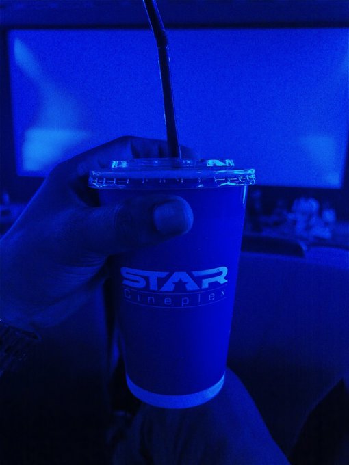 https://i.imgur.com/Movie theater placeholder. Actually: A hand holding a blue-lit "STAR Cineplex" cup with a straw in a darkened movie theater.