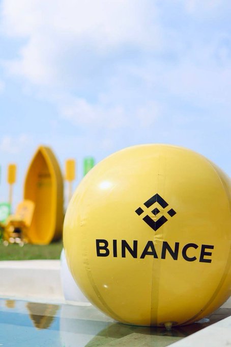 A large yellow inflatable ball prominently displays the Binance logo and name, with an outdoor event setup blurred in the background.