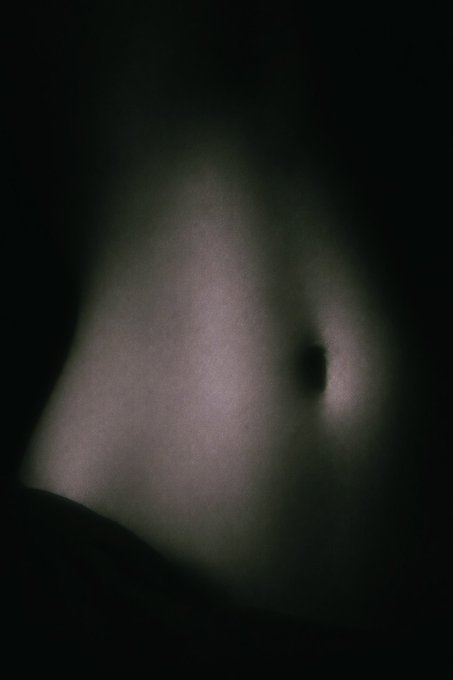 A dark, blurry, abstract image showing a small dark focal point emerging from a hazy, dimly lit grayish background.