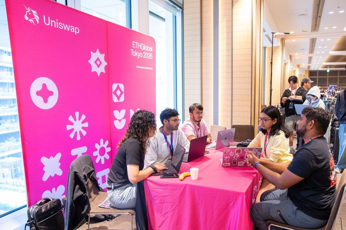 Attendees gather at a pink Uniswap booth during ETHGlobal Tokyo 2026, with team members discussing around laptops at the conference table.
