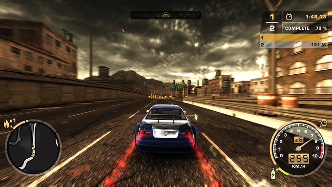 A screenshot from a racing video game showing a silver sports car driving at 233 km/h down a highway under cloudy skies, with a race position tracker showing '1' and '2 COMPLETE 70%' and a mini-map in the corner.