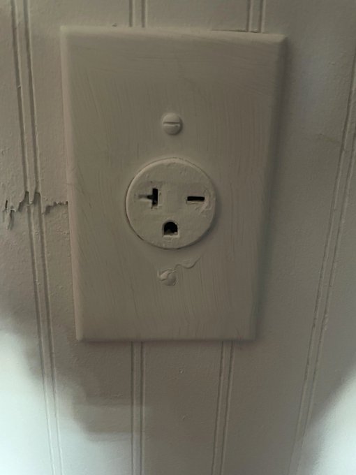 A close-up photo of a worn, painted gray electrical wall outlet showing visible drip marks on the surrounding wood paneling.