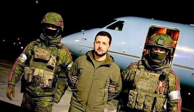 A man in a green jacket is escorted by two armed soldiers in camouflage uniforms and helmets with orange-and-black striped ribbons, standing in front of an airplane at night.