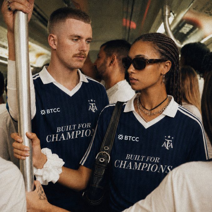The image shows a man wearing a blue shirt with white text that says "BTCC" and another man wearing sunglasses, possibly a woman, who are standing close together. The background of the image features other people as well. There is also an object in the scene, which appears to be a handbag or purse held by one of the individuals present.

The post seems to be promoting a sports event or competition involving teams from Argentina and France. It could be related to the World Cup, given that it mentions "FIFAWorldCup". The image captures an interesting moment between two people who are likely discussing their shared interest in the event.