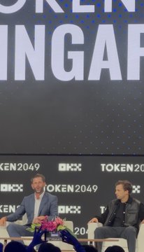 Two men sit on stage at the TOKEN2049 conference (as shown on the large backdrop and repeated logos) for what appears to be a panel discussion, likely capturing the "incredible talks from the legends" mentioned in the post, with the "Token2049 is coming to New York in 2027" announcement tying into the speaker's enthusiasm.