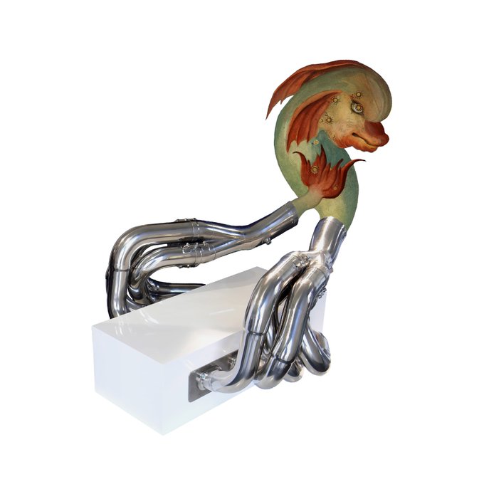 A sculptural object featuring metallic exhaust pipes supporting a green, fleshy creature with leaf-like appendages.