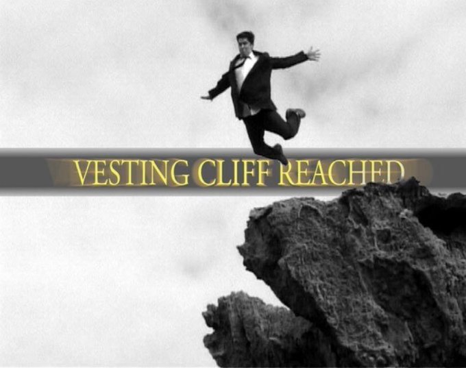 A black-and-white meme showing a man jumping across a cliff with the text "VESTING CLIFF REACHED" overlaid in gold.
