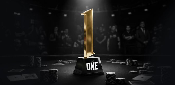 A golden number one trophy labeled 'ONE' stands on a podium illuminated by a spotlight, with poker chips, playing cards, and an audience in the dark background.
