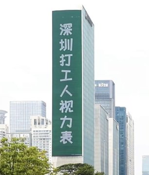 A tall skyscraper in an urban setting displaying a large vertical green LED screen with Chinese text reading '深圳打工人视力表' (Shenzhen Workers' Vision Chart).