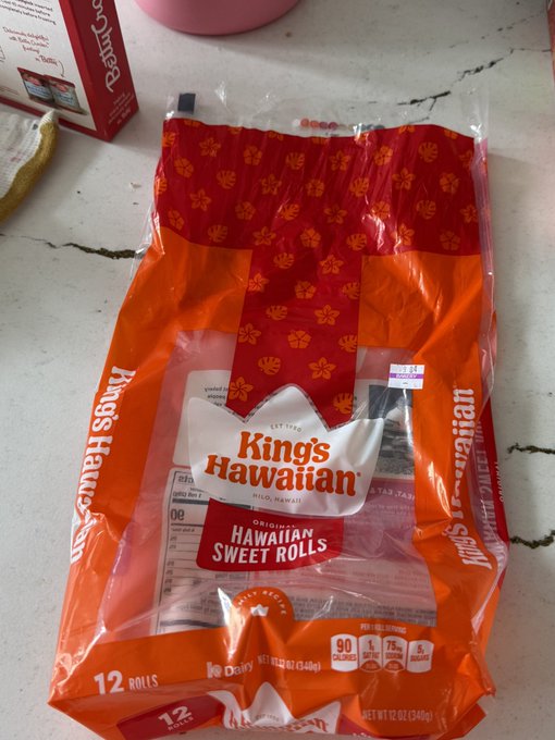 An orange plastic bag of King's Hawaiian Original Hawaiian Sweet Rolls sits on a white marble countertop, branded with 'Hilo, Hawaii' and noting a 12-roll count and a 1.29 price tag.
