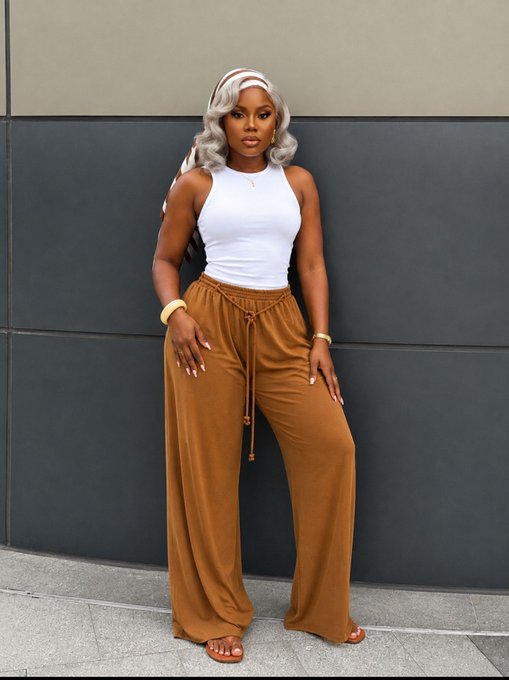 A fashion photo of a woman modeling a white halter crop top paired with loose, rust-colored drawstring pants and a matching headscarf.